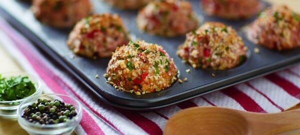 A muffin tin filled with round spiced Turkey Meatballs, and a nearby wooden spoon.