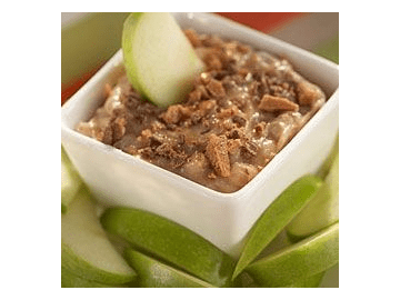 A square white bowl filled with toffee apple dip, and slices of Granny Smith apples.