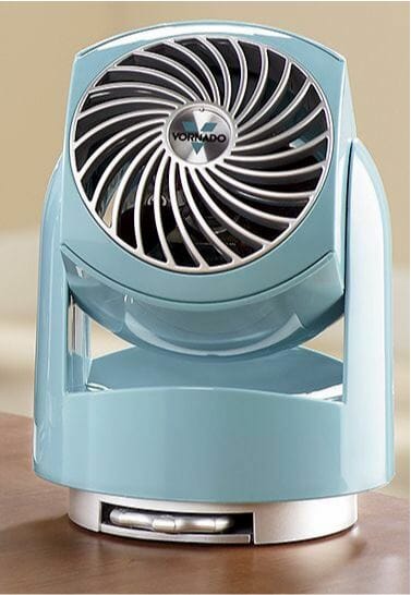 A blue Vornado desk fan, placed on a wood surface.
