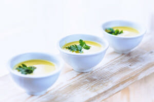 Three white bowls of Pumpkin Soup, with parsley sprig garnishes.