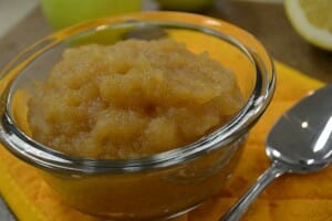 A clear bowl of homemade applesauce with cinnamon and brown sugar, with a spoon nearby.