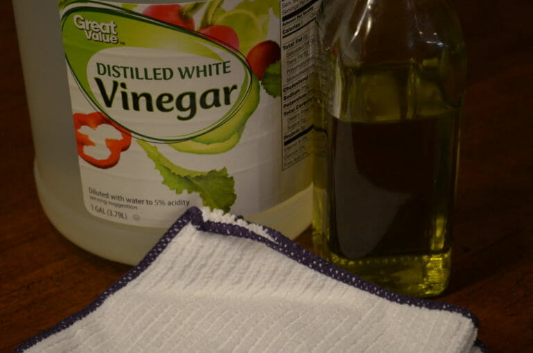 A bottle of white vinegar, a bottle of another liquid, and a white folded dish cloth.