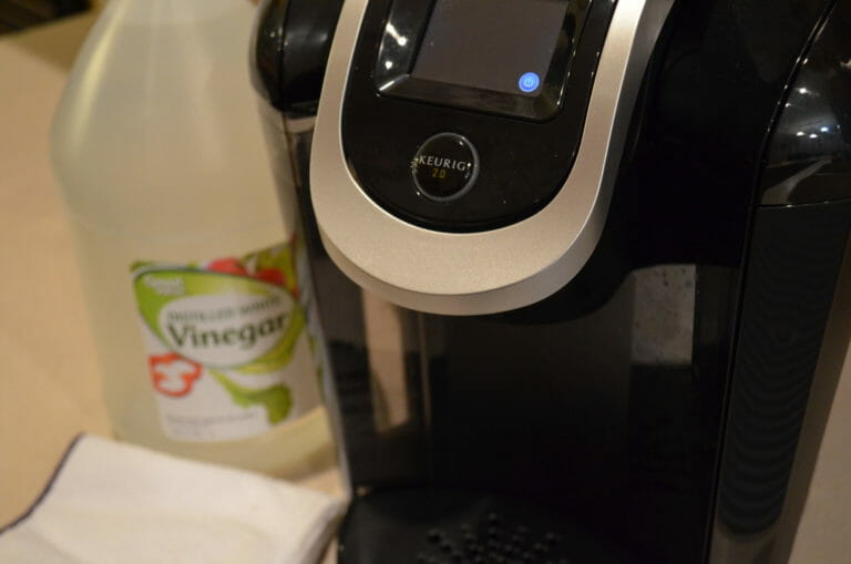 A black Keurig brand coffee maker, with a bottle of white vinegar and a folded white dish cloth.