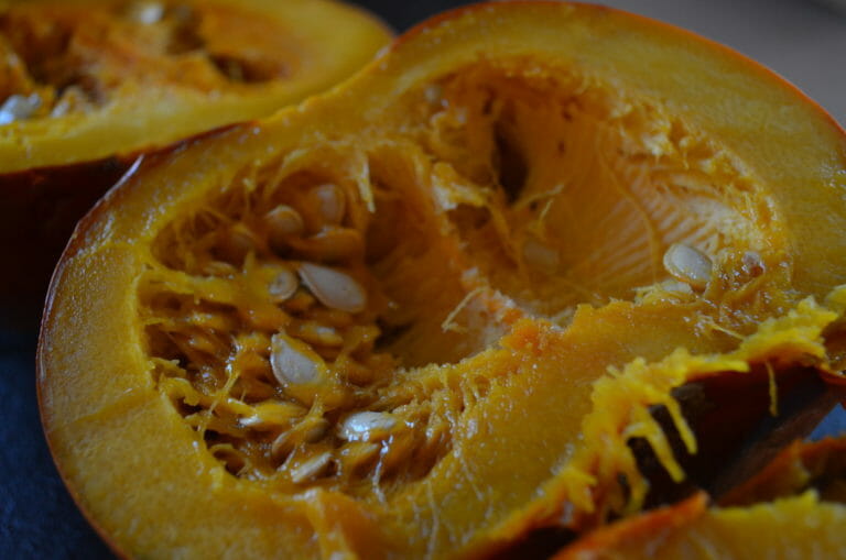 Close-up of a half small cooked pumpkin, exposing the seeds.