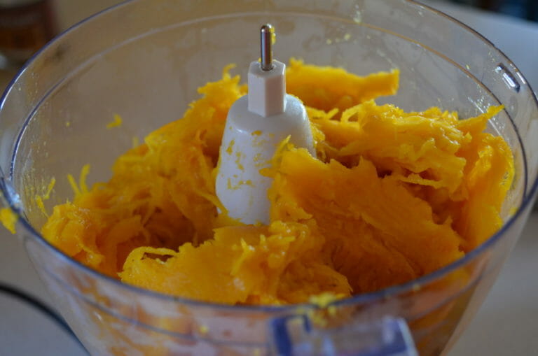 Close-up of cooked pumpkin pieces in a food processor bowl.