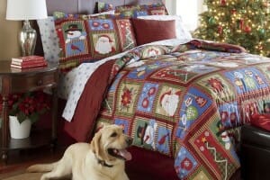 A comforter set with a patchwork look of Christmas themes, a blonde Lab Retriever, and a live decorated tree.