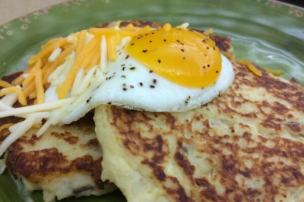 A green plate with a serving of two potato pancakes topped with a sunny-side-up egg and shredded cheese.