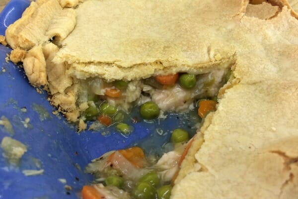 Close-up of a blue pie plate filled with a Turkey Pot Pie with a slice removed, exposing the peas, carrots, and turkey.