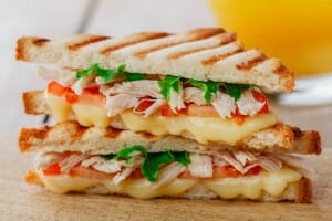 Two halves of a grilled Turkey Sandwich stacked, showing melted cheese, tomato, turkey, and lettuce.