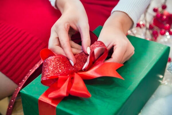 Close-up of a woman tying a red bow onto a green wrapped present.
