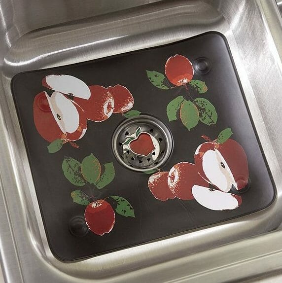 A black sink mat decorated with whole and sliced red apples with green leaves.