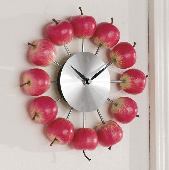 A brushed chrome wall clock with 3D red apples to mark the hours.