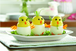 Three Deviled Eggs in the shape of chicks popping out of a white egg, with carrot wings and beaks, and black olive eyes.