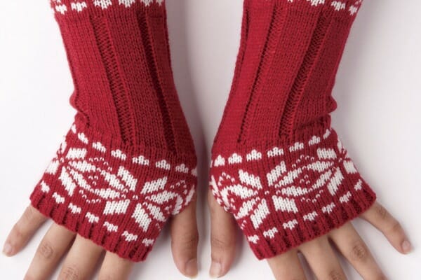Hands wearing red knit fingerless gloves with a white snowflakes design.