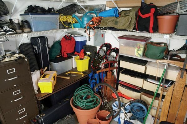 A cluttered storage area with garden items, tools, a sled, shoes, a file cabinet, and more.