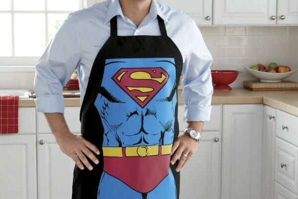 A man in a kitchen wearing a Superman apron.