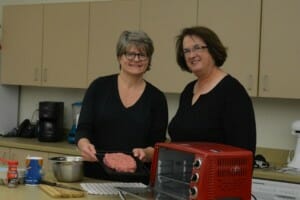 Ginny and Lisa, both in black tops, in a kitchen with Ginny's brand small appliances.