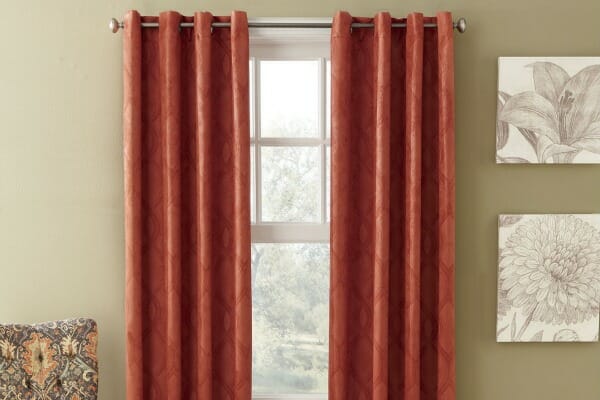 Spice colored grommet blackout curtains hung over a window, next to two floral wall canvases.