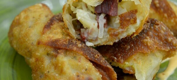 A green plate holding fried Reuben Rolls, with one opened to show the Reuben ingredients.