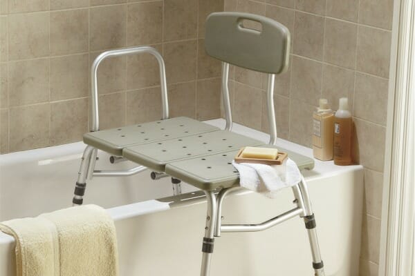 A gray and chrome medical transfer bench partially in a bathtub, with a handle on one side.