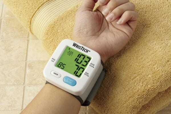 A person's hand resting on a folded yellow towel, wearing a wrist blood pressure monitor.