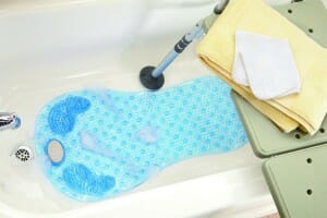 A bath chair in a tub with a blue bath mat in the shape of a foot, with several suction cups for safety.