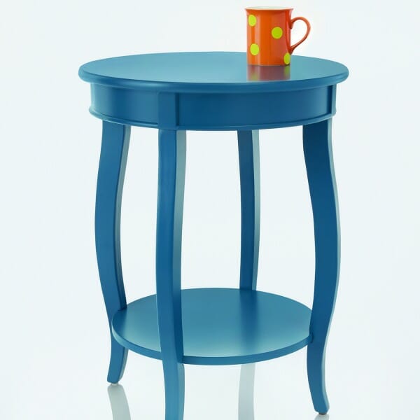 A blue round side table with an orange mug with lime dots placed on top.