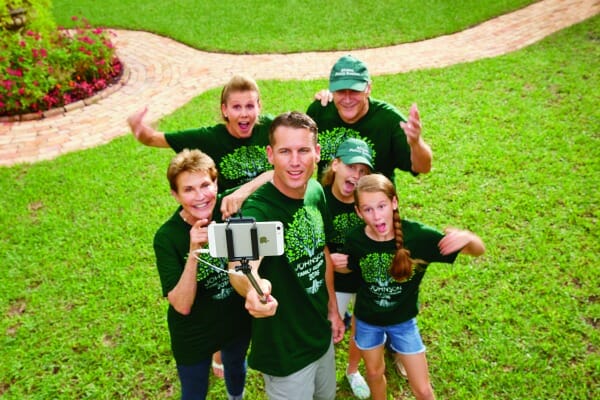 Six people wearing green family reunion T-shirts grouped together, with one holding a selfie stick for a group photo.