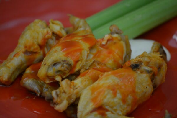 A red plate filled with Hot Wings topped with a red sauce, with celery on the side.