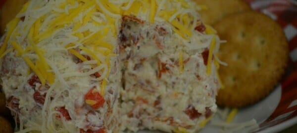 A red and white bowl filled with round crackers and a Pepperoni Cheese Ball topped with shredded cheese.