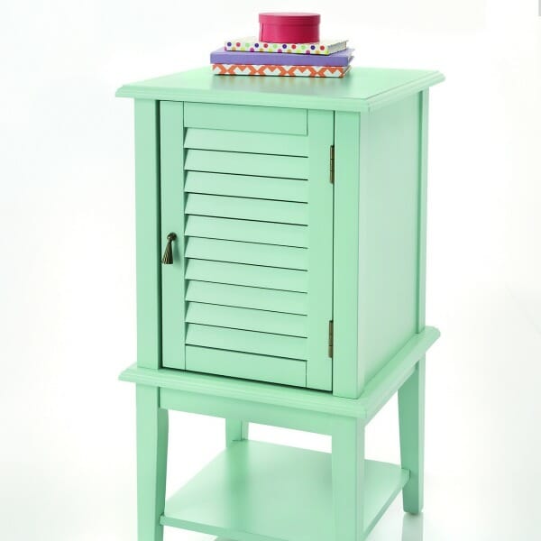 A seafoam green side table with a bottom shelf and a shutter door, with books placed on top.