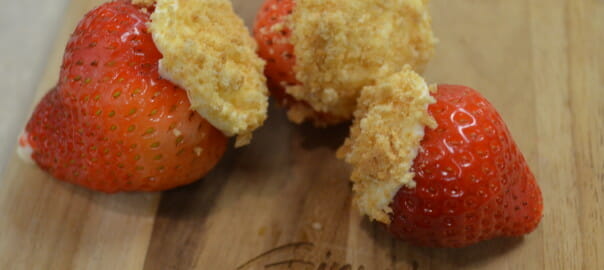 Three strawberries on a Ginny's cutting board, stuffed with Cheesecake Filling and topped with graham cracker crumbs.