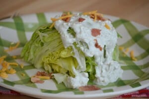 A green and white plate with a lettuce wedge topped with Bacon Bleu Cheese Dressing.