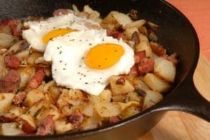 A black cast iron pan filled with fried Corned Beef Hash topped with two sunny-side-up eggs.