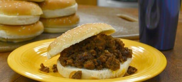 A yellow plate with a Sloppy Joe sandwich, and a stack of buns in the background.