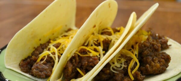A green plate with three soft shell tacos topped with shredded cheese.