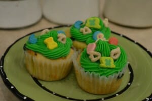 Three cupcakes on a green plate, decorated with green frosting and Lucky Charms cereal and marshmallows. 