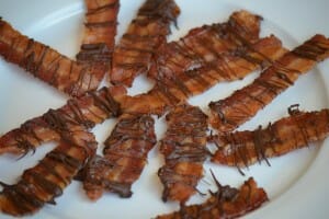A white plate filled with chocolate drizzled candied bacon.