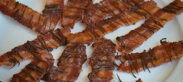 A white plate filled with chocolate drizzled candied bacon.