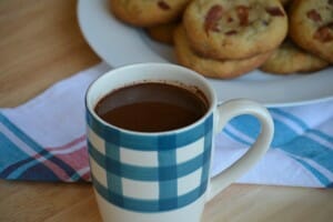 A blue and white mug filled with Slow Cooker Bacon Hazelnut Hot Chocolate, next to a plate filled with cookies.