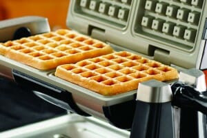 A waffle iron with two golden waffles inside.