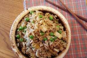 A round brown and white bowl filled with Fried Rice with Veggies, and a pair of chopsticks on the side.