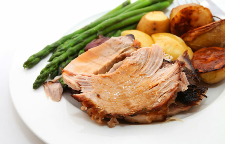 A white plate filled with juicy pork tenderloin, asparagus, and roasted potatoes.