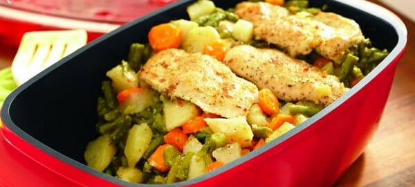 A red baking dish filled with chicken and vegetables, with a portion removed.