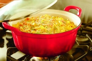 A red casserole dish with a clear lid on a gas stove, filled with Tuna Casserole.