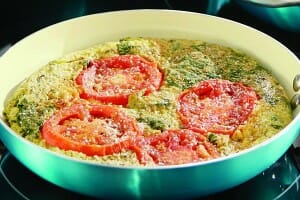 A blue and white skillet filled with Veggie Frittata that is topped with sliced tomatoes and Parmesan cheese.