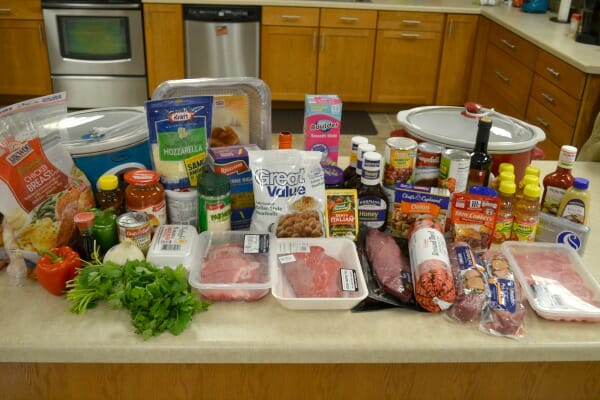 A kitchen counter filled with packaged groceries, including meats, vegetables, condiments, cheeses, and eggs.
