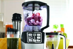 A berry filled Ninja food processor with accessories, including a blending cup filled with a green beverage.