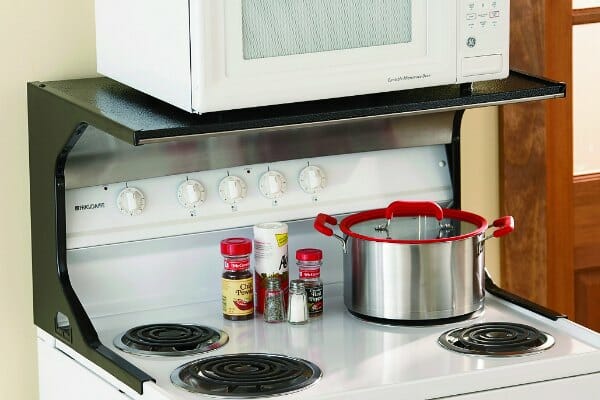 A white electric stove with an attached black oven shelf that is holding a white microwave oven.
