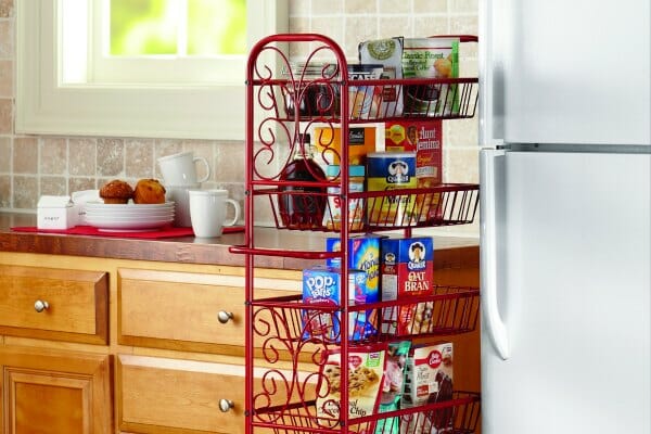 A thin red-scrolled, rolling metal pantry that fits in the space between kitchen cupboards and a refrigerator.